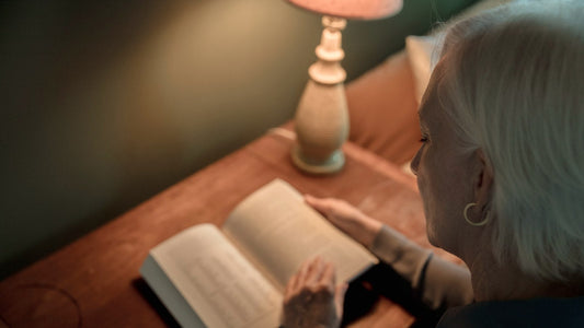 Woman with silver hair reading a book by the warm light of a table lamp on an autumn evening